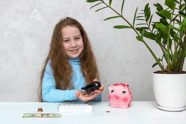 Photo happy little girl pours coins from her purse into her palm on the table in front of her is a calculator money piggy bank