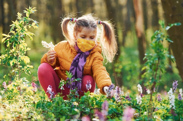 Happy little girl in protective mask sitting in spring forest at daytime