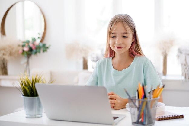 Happy little girl pupil using laptop at home