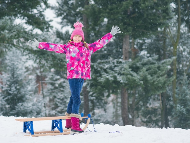 Foto piccola ragazza felice in slitta e divertita bambino che gioca all'aperto in slitta sulla neve bambino che slitta nel parco innevato in inverno divertimento all'aperta per le vacanze natalizie dell'infanzia