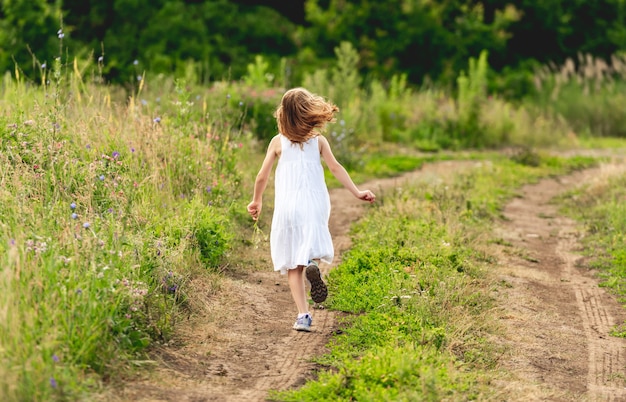 Happy little girl running along ground path outdoors. back view