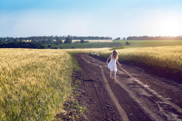 Happy little girl running on a dirt road in the fields. Ukrainian landscape