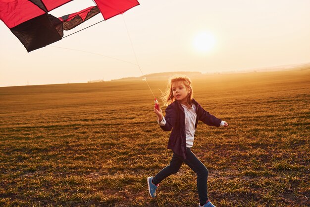 Happy little girl running with kite in hands on the beautiful field at sunrishe time