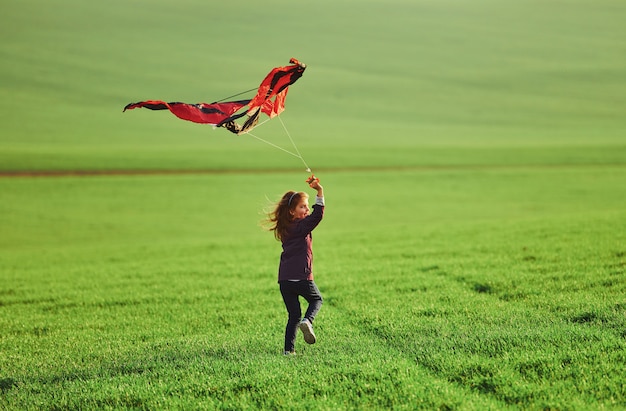 Happy little girl running with kite in hands on the beautiful field