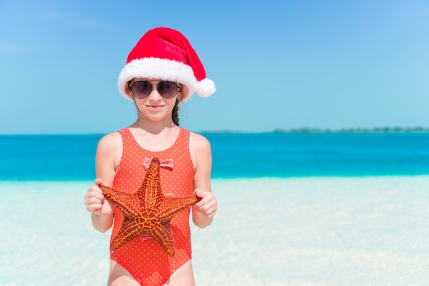 La bambina felice in cappello di santa durante le vacanze al mare di natale si diverte molto