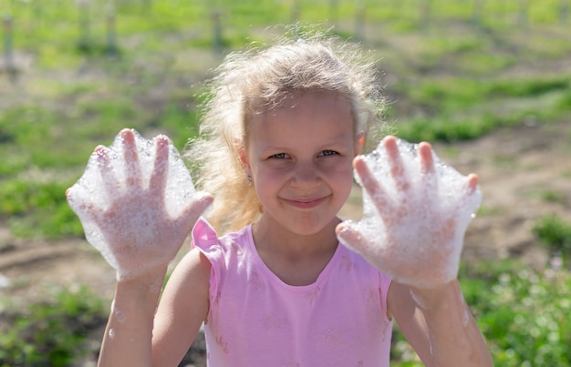 happy little girl showing hands with soapy foam foam party