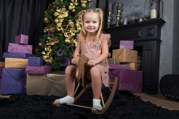 Happy little girl sitting on a swing in the shape of a horse in the New Year decor