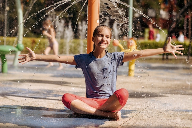 Happy little girl sitting in yoga pose on water playground in summer park. Child leisures in aquapark