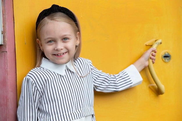 A happy little girl smiles at the camera against the yellow wall