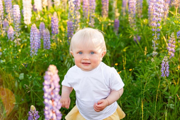 Happy little girl smiling outdoor. Beautiful blond young baby girl resting on summer field with blooming wild flowers green background