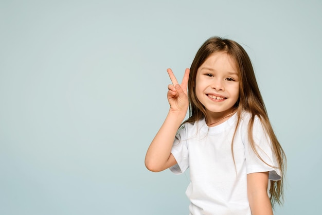 青い背景にVピースサインの手のジェスチャーを見せて微笑む幸せな女の子世界への平和は戦争を止める