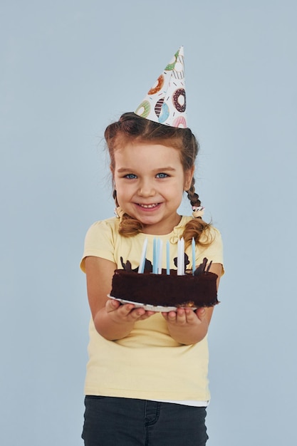 Foto bambina felice in piedi e divertirsi al chiuso alla festa di compleanno con la torta
