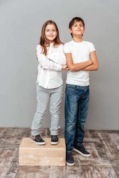 Happy little girl standing with arms crossed on box near tall smiling boy