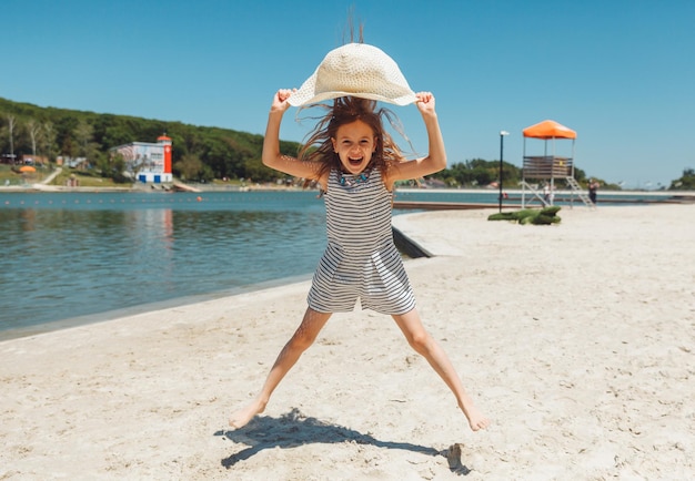 Happy little girl in a straw hat jumping on the beach in summer vacation