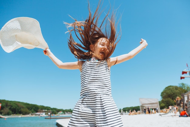 여름 방학에 해변에서 점프하는 밀짚 모자를 쓴 행복한 어린 소녀