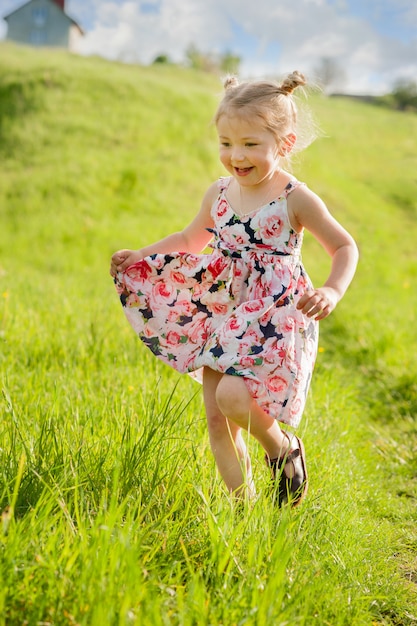 A happy little girl in summer dress with pigtails run in a green field