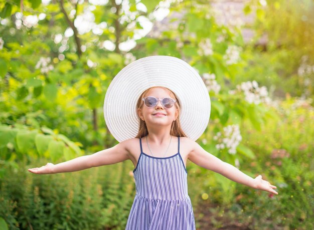 Photo happy little girl in sunglasses and hat in the garden with holiday summer and freedom concept