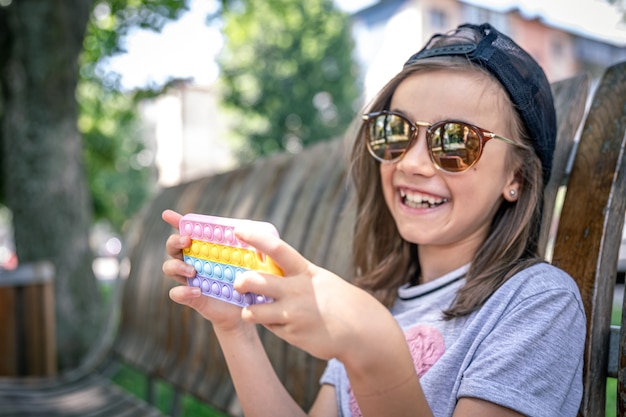 Happy little girl in sunglasses with a smartphone in a trendy case pop it