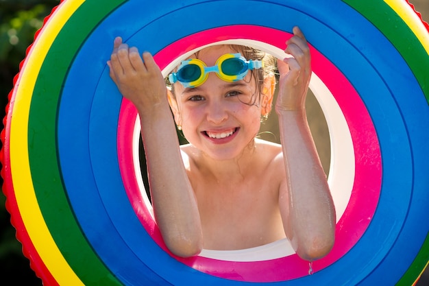 Photo a happy little girl in swimming glasses and a colorful inflatable ring