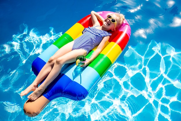 La bambina felice nuota in piscina in estate su un materasso a forma di spazio gelato per il testo