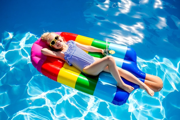 Happy little girl swims in the pool in the summer on a mattress in the form of ice cream space for text