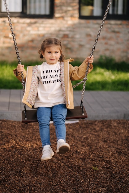 Photo happy little girl swing on a swing in the specially designated place in the park softner from