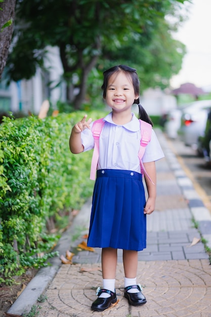 Happy little girl in Thai school uniform with backpack standing in the park