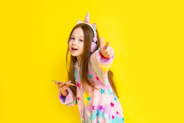 Bambina felice in un unicorno kigurumi su uno sfondo giallo