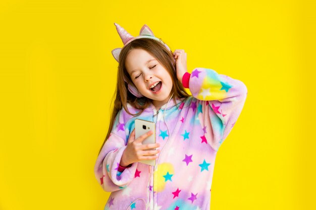 Happy little girl in a unicorn Kigurumi on a yellow background