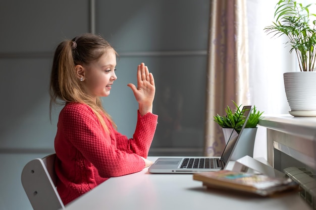 Happy little girl using laptop at home for lessons on online education and home studying. Kids distance learning. Social distance. Stay at home.