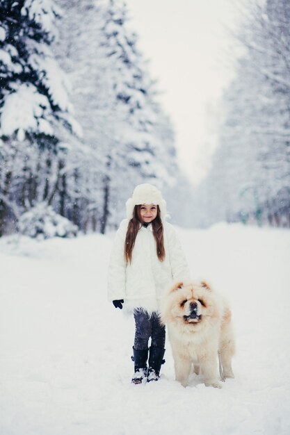 Happy little girl walking with a dog in a snowy park