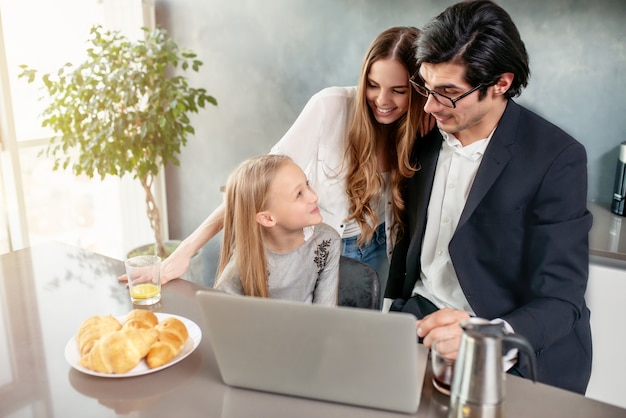 Photo happy little girl watching a movie on the computer with her father and mother