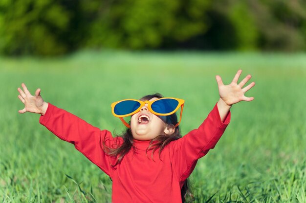 Happy little girl wearing big sunglasses with hands up enjoying sun in the field