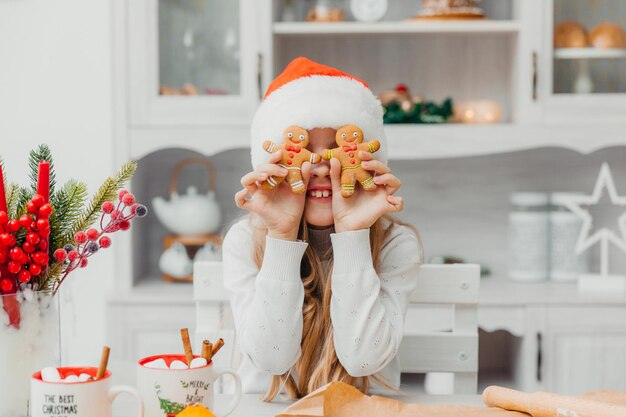 Happy little girl wearing santa claus hat holds gingerbread men.