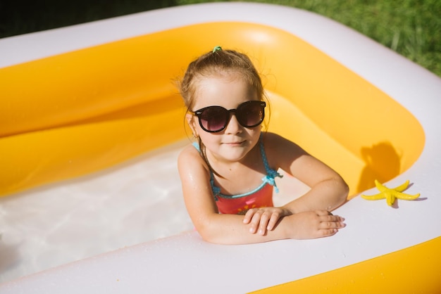 Happy little girl wearing sunglasses and swimsiut in the inflatable pool at the sunny day