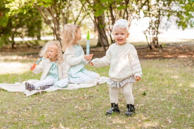 Photo happy little girl in white tights and headbands on a picnic with her sisters the baby is learning to walk