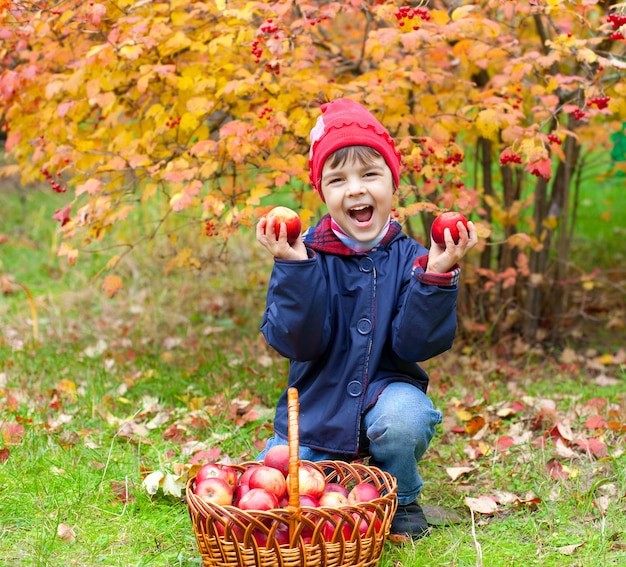 Счастливая маленькая девочка с яблоками в саду