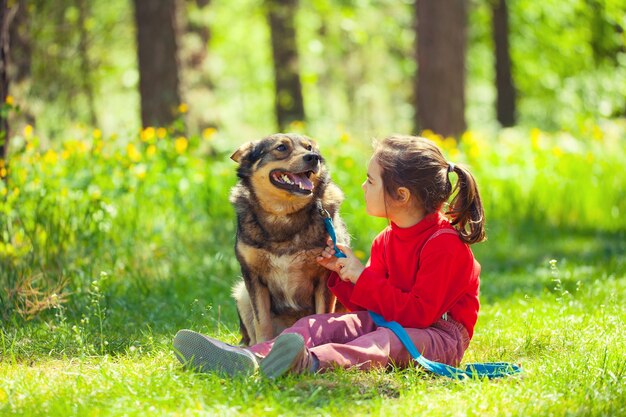 Bambina felice con un grosso cane seduto nel prato