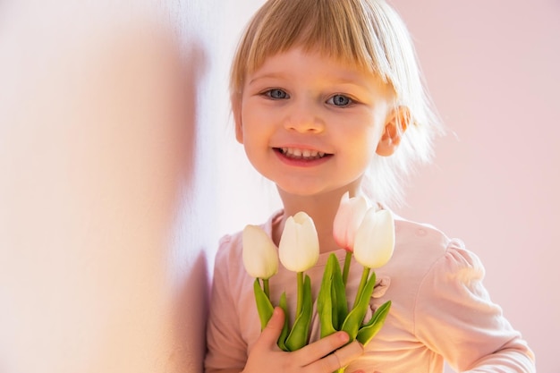 日当たりの良い部屋で手にカラフルなチューリップの花束を持っているブロンドの髪の幸せな少女