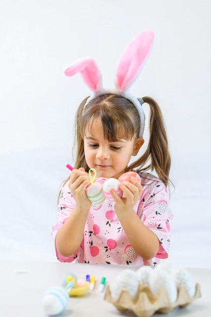 Happy little girl with bunny ears painting the egg with fiberpen preparing for Happy Easter day