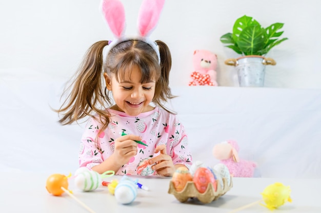 Bambina felice con le orecchie del coniglietto che dipinge l'uovo con la penna di fibra che si prepara per il giorno di pasqua felice