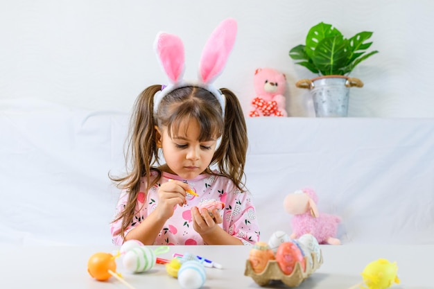 Happy little girl with bunny ears painting the egg with fiberpen preparing for Happy Easter day