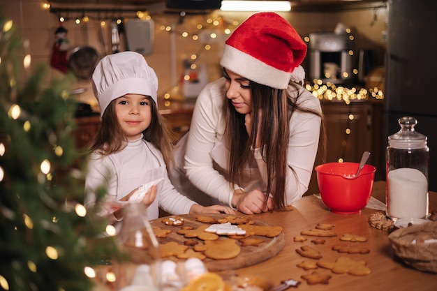 Happy little girl with her beautiful mom make gingerbread at home christmas decoration at kitchen