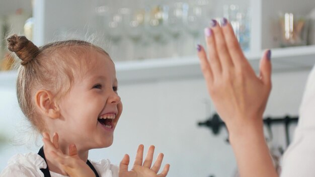 Photo happy little girl with her mother clap their hands in the kitchen