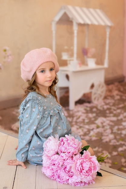 happy little girl with long curly hair in beret with a bouquet of peonies in french vintage cafe