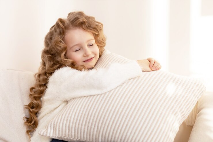 Happy little girl with long hair hugging a pillow and smiling
