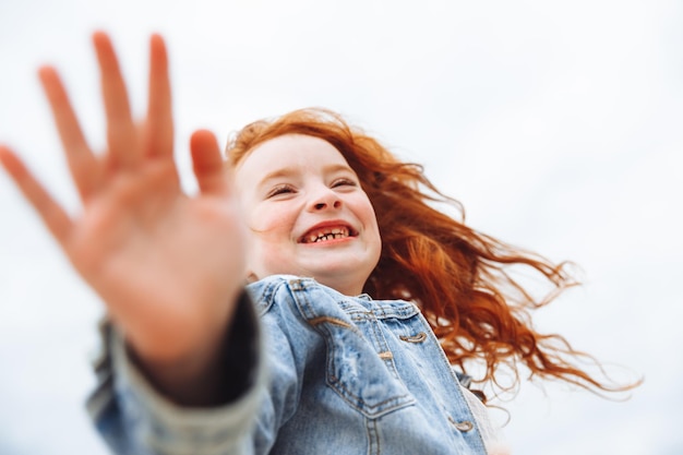 Счастливая маленькая девочка с рыжими волосами бежит по пляжу