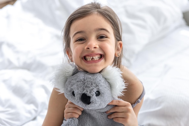 Bambina felice con il koala di peluche a letto