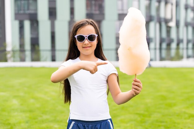 Happy little girl with sweet cotton candy in summer park.