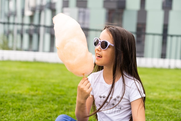 Happy little girl with sweet cotton candy in summer park.